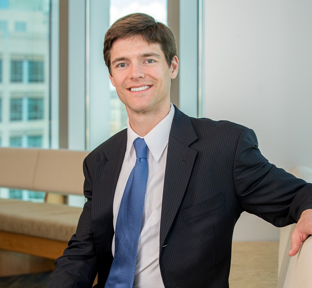 a young man with brown hair wearing a dark suit a blue tie