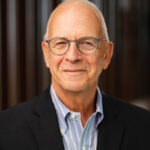 Professor Amos Guiora, a white man with grey hair wearing round-rimmed glasses and a blue-and-white-striped button-up and navy blazer