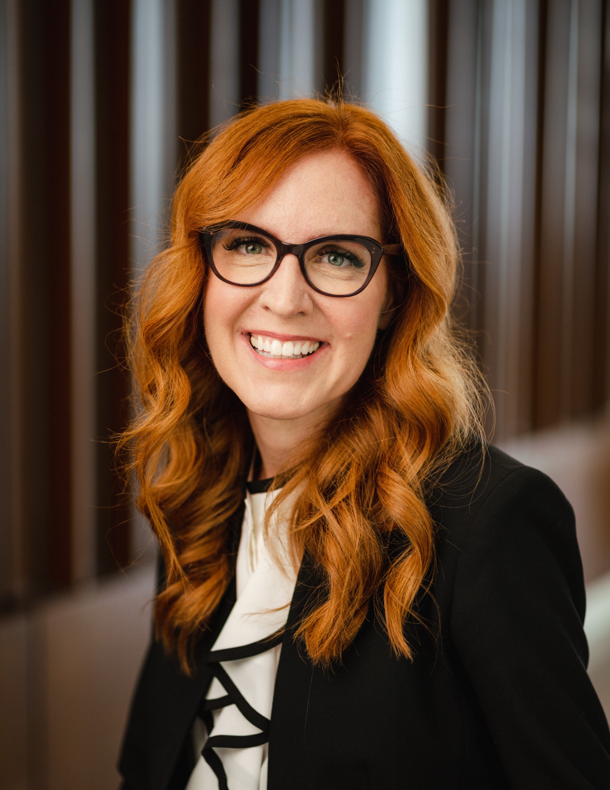 Professor RonNell Andersen Jones, a white woman with long, wavy red hair wearing glasses and a black blazer
