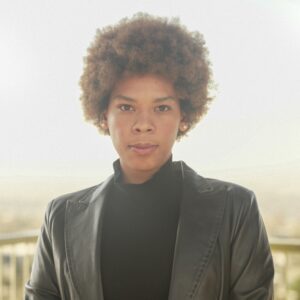 Arin Perkins, a young Black woman with short, curly brown hair wearing a black turtleneck and black leather blazer