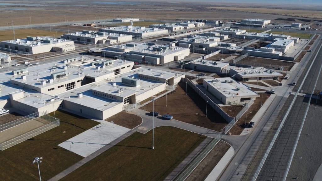 Exterior of the Utah State Correctional Facility west of Salt Lake City with several white buildings connected to each other amid a flat desert landscape