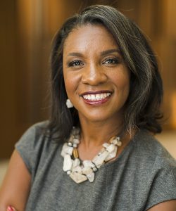 Professor Erika George, a black woman wearing a grey blouse and white stone necklace