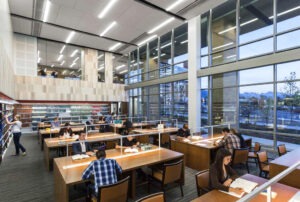 Light-filled interior of S.J. Quinney College of Law building, with students sitting at wood desks studying adjacent to a grid of windows