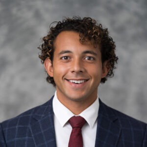 Joey Sandres, a young man with curly dark-brown hair and brown skin wearing a navy blue blazer and burgundy tie