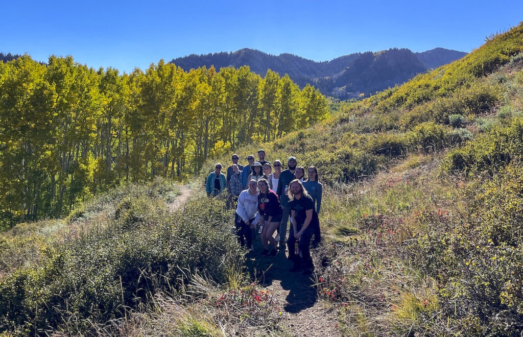 Students and featured speakers stand together near trees with golden yellow leaves in Northern Utah