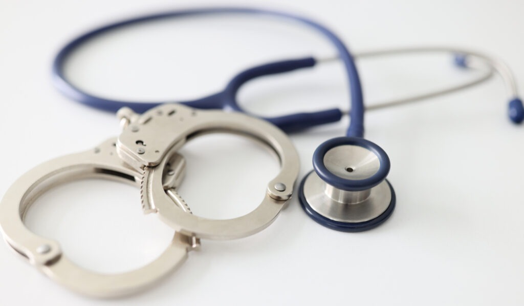 Handcuffs and a stethoscope on a white background, close-up.